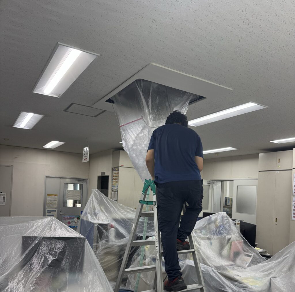 脚立に乗って天井カセット形エアコンを洗浄するスタッフ